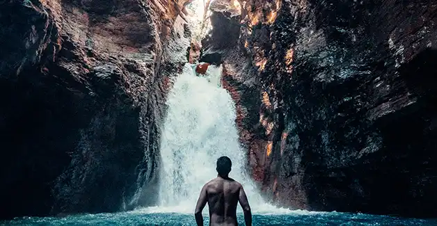 Um homem de pé na água em frente a uma cascata.