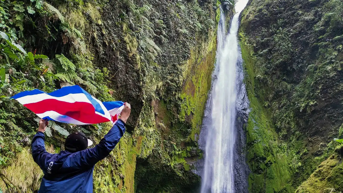 Um homem segura uma bandeira em frente a uma cascata.
