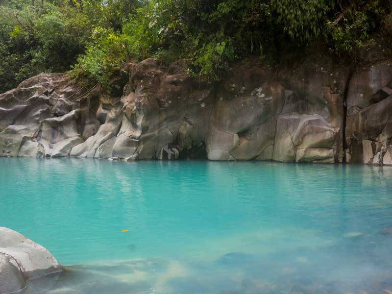 Uma piscina de água azul rodeada de rochas e árvores.