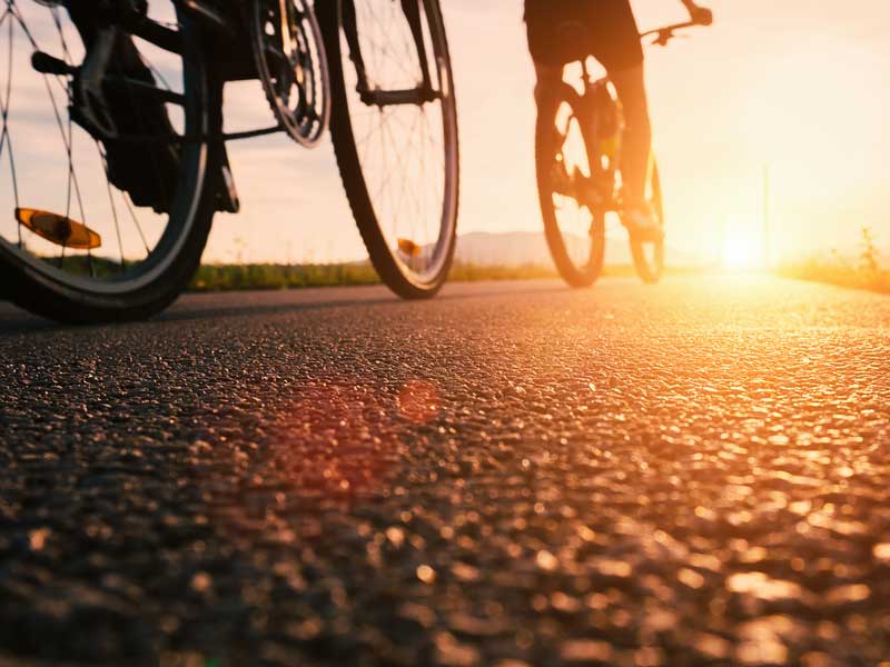 Uma pessoa a andar de bicicleta numa rua ao pôr do sol.