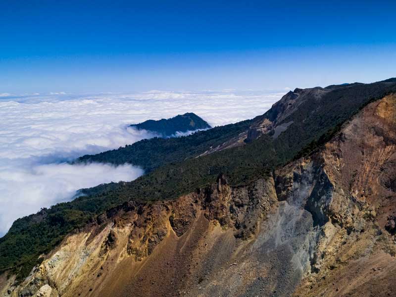 Uma vista do cimo de uma montanha com nuvens por baixo.