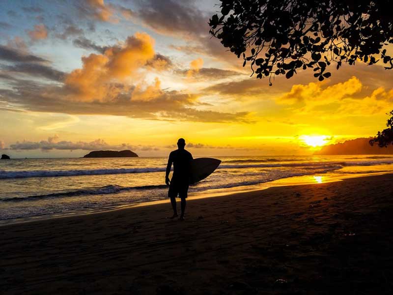 Um homem a segurar uma prancha de surf numa praia.