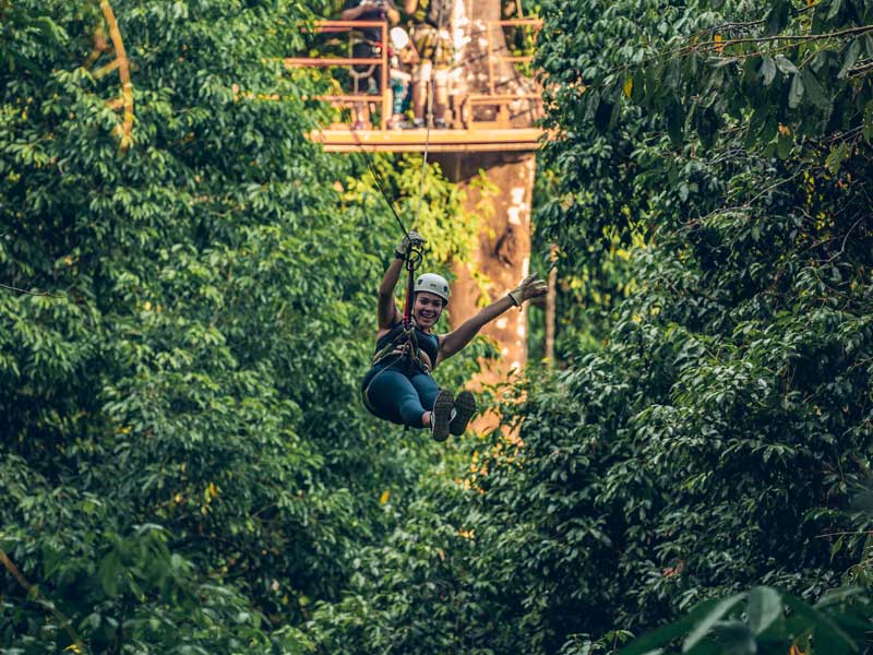 Uma mulher a andar numa tirolesa no meio de uma floresta.