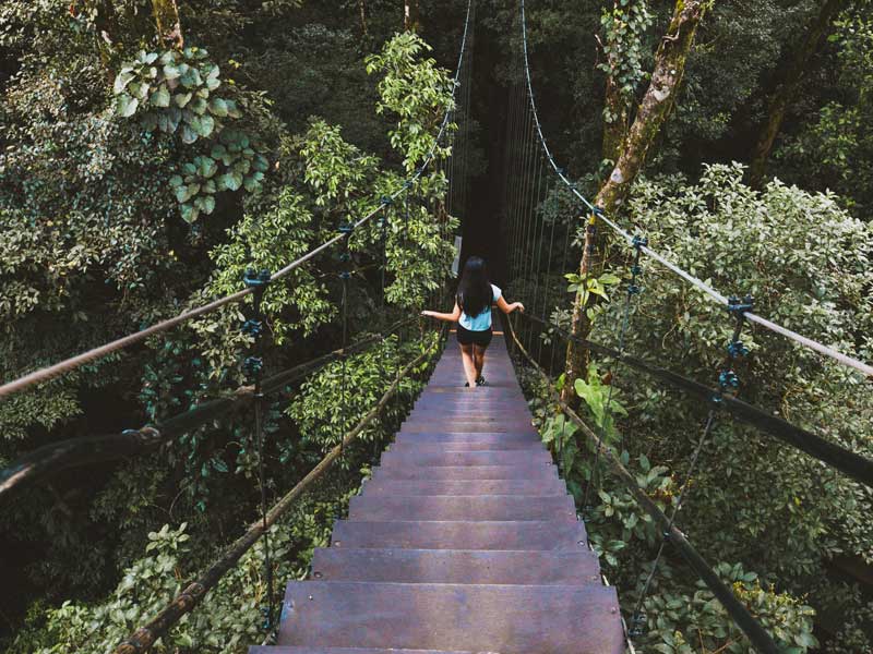 Uma mulher a atravessar uma ponte suspensa na selva.