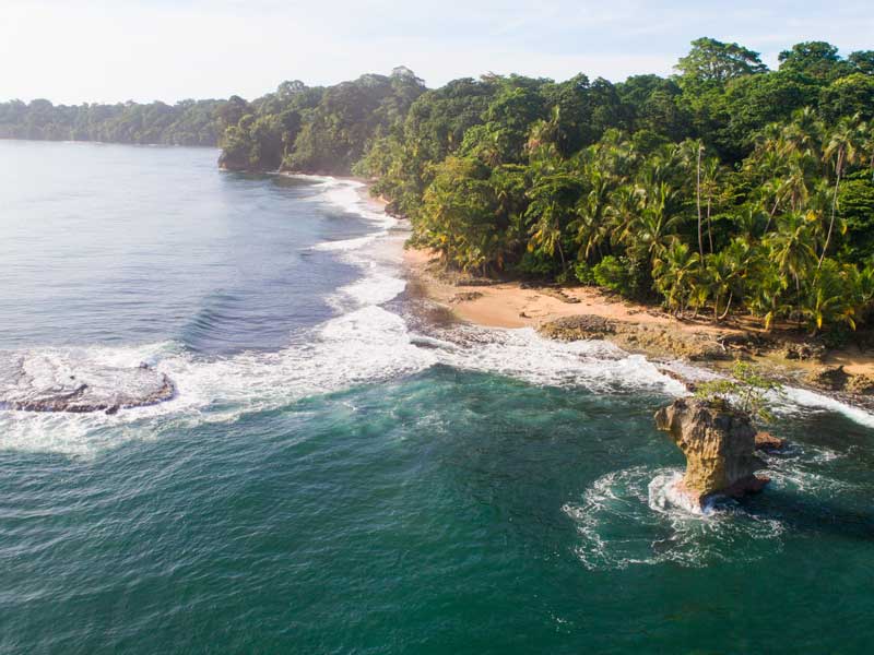Uma vista aérea de uma praia com uma rocha no meio do oceano.