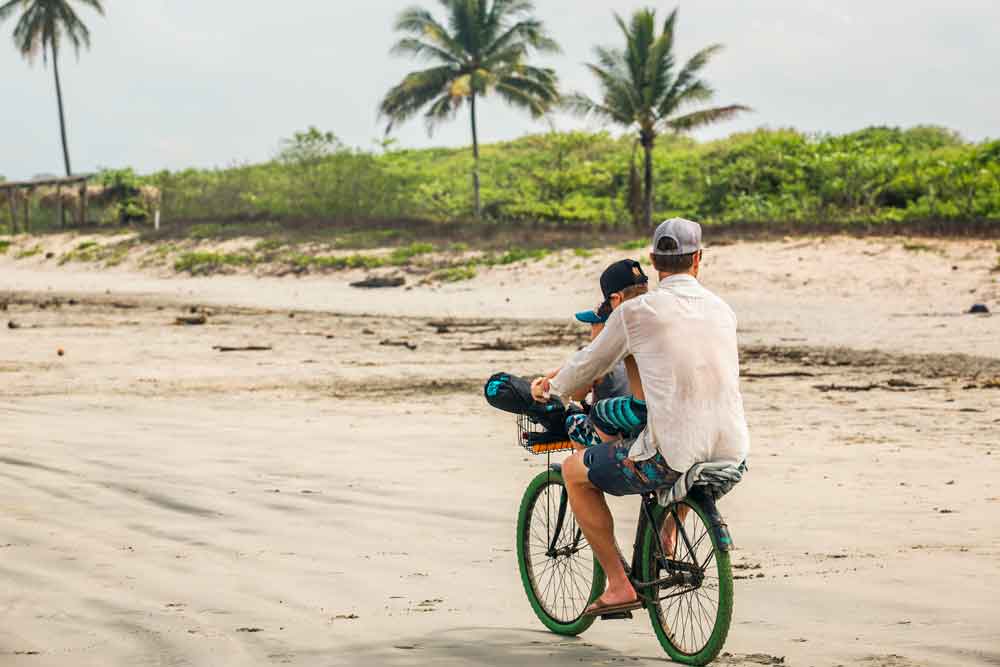 Um homem e um rapaz a andar de bicicleta numa praia.