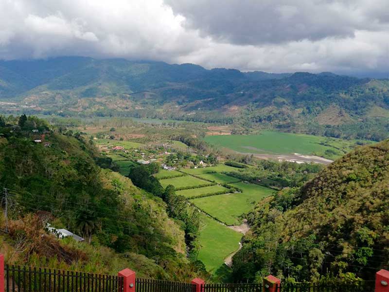 Um vale verdejante rodeado de montanhas sob um céu nublado.