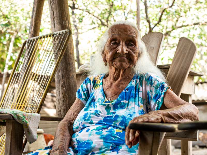 Uma mulher idosa sentada numa cadeira no exterior.