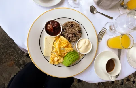 prato com alimentos de pequeno-almoço numa mesa, acompanhado de café e sumo de laranja
