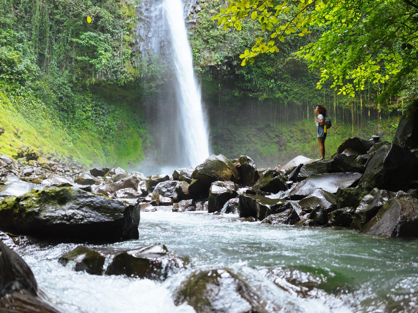 Mulher em pé ao lado de uma cascata na selva