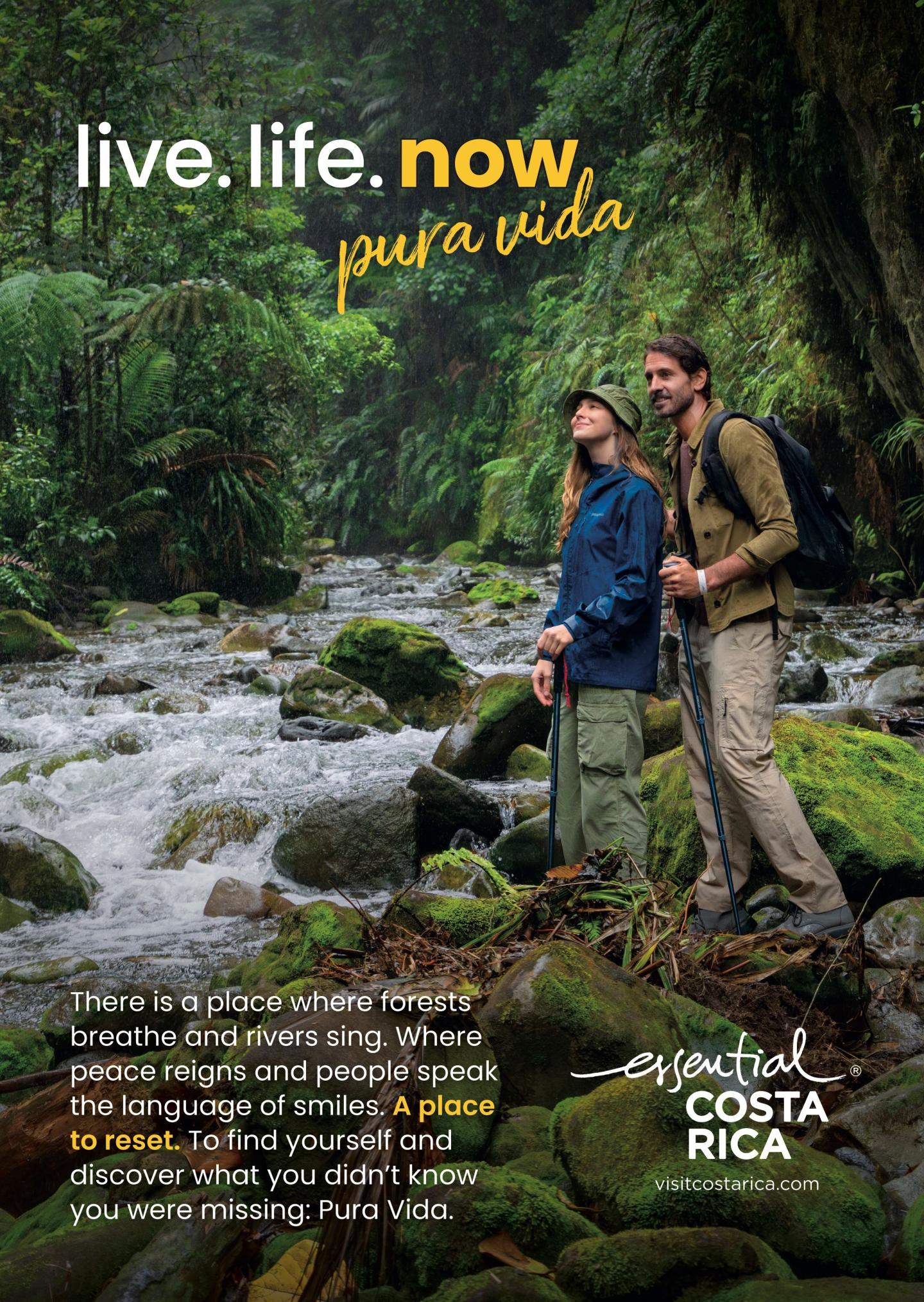 Anúncio que mostra dois caminhantes em pé sobre rochas cobertas de musgo junto a um rio, numa exuberante floresta tropical. Título: «live.life.now» epura vida». O texto descreve florestas que respiram, rios que cantam e uma oportunidade para recarregar baterias. Logótipo: «esencial Costa Rica, visitcostarica.com.